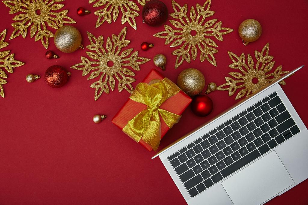 Top view of laptop near wrapped present and decorations on red background  - Photo, Image