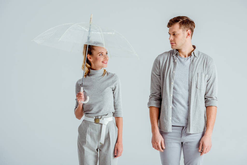 usmívající se žena držící transparentní deštník a při pohledu na pohledný muž izolované Grey - Fotografie, Obrázek