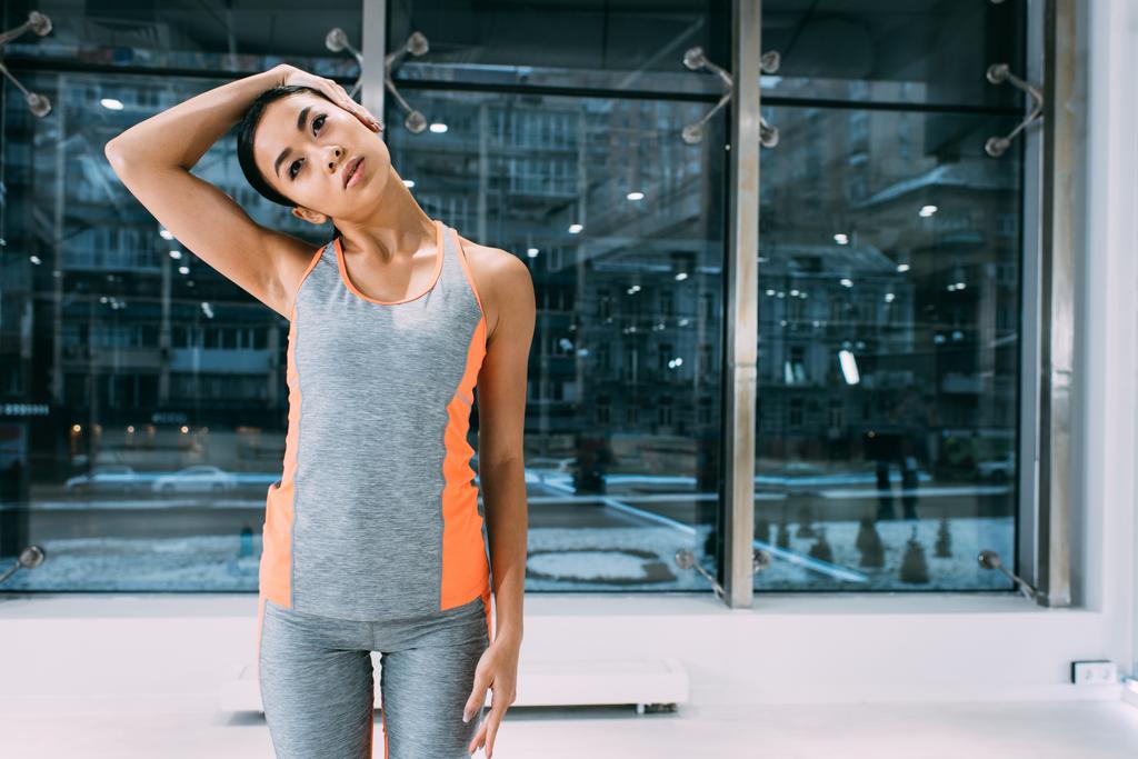 стройная азиатская девушка, стоящая и растягивающая шею в спортзале
 - Фото, изображение