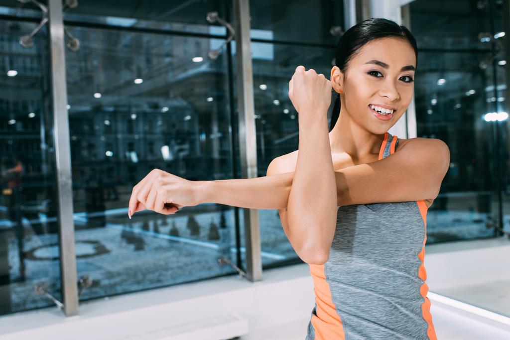 Nahaufnahme eines lächelnden asiatischen Mädchens, das die Hand ausstreckt und im Fitnessstudio in die Kamera schaut - Foto, Bild