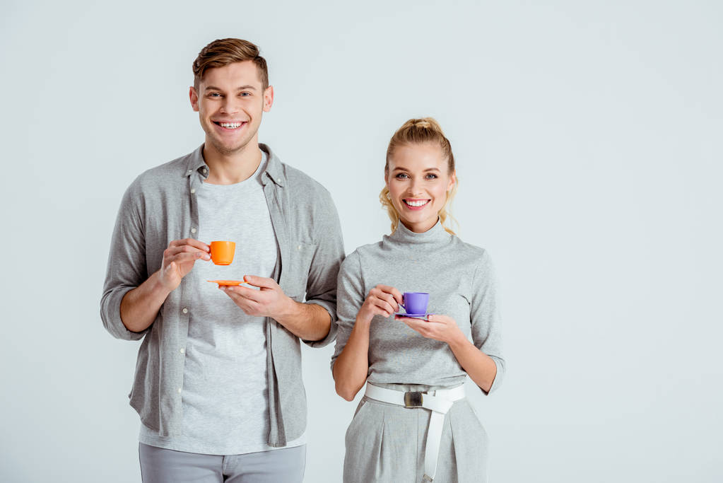 улыбающаяся пара, держащая чашки кофе и глядя на камеру, изолированную на сером
 - Фото, изображение