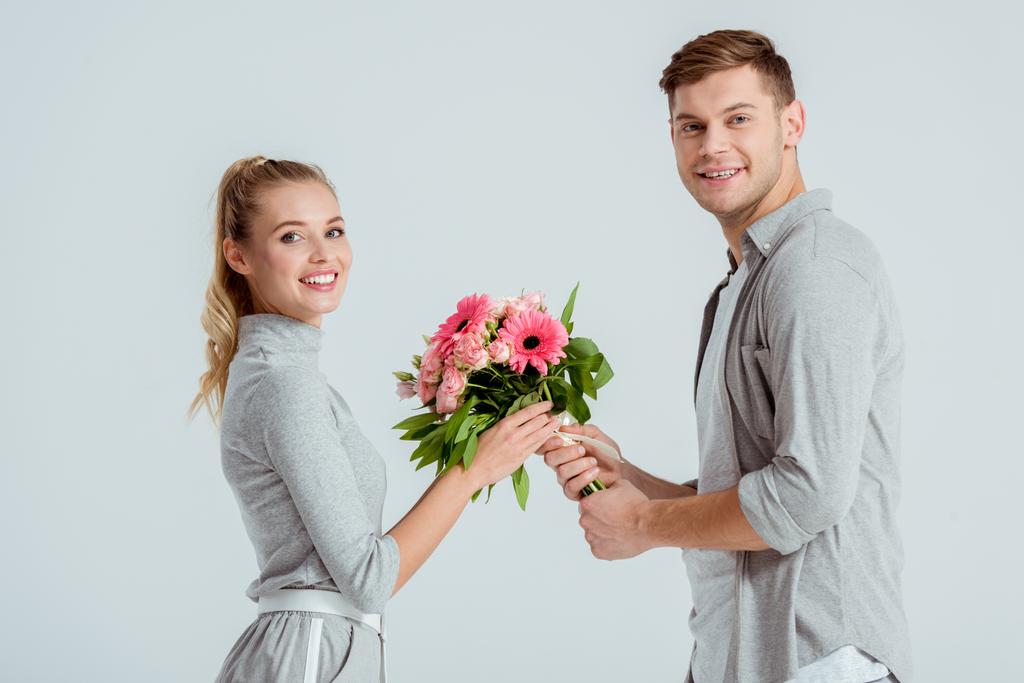 bonito homem dando buquê de flores para bela mulher sorridente isolado no cinza
 - Foto, Imagem