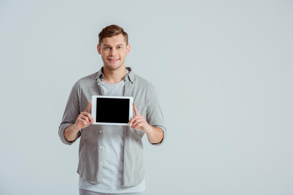 pohledný muž v šedém oblečení při pohledu na fotoaparát a prezentaci digitálních tabletu s prázdnou obrazovkou izolované Grey - Fotografie, Obrázek