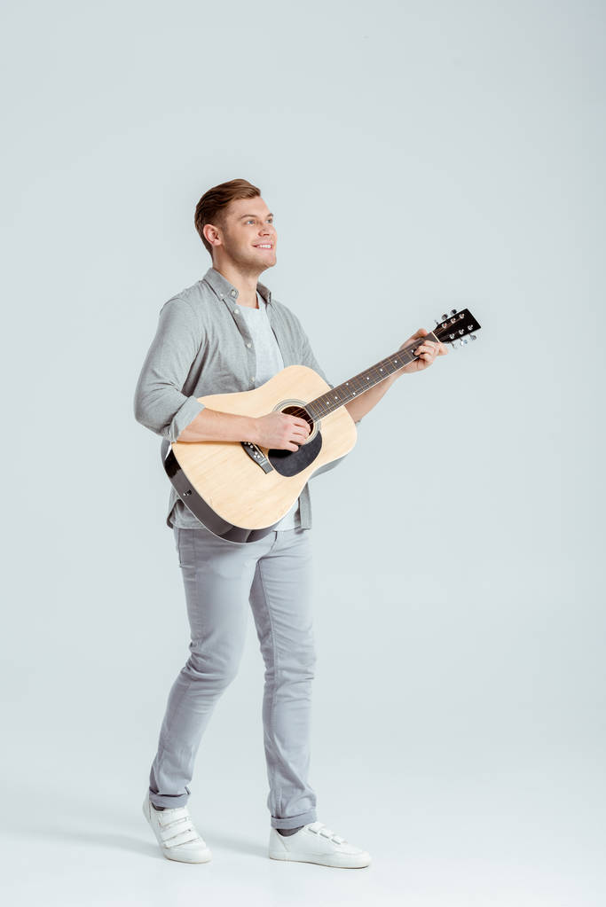 handsome man in grey clothing playing acoustic guitar on grey background - Photo, Image