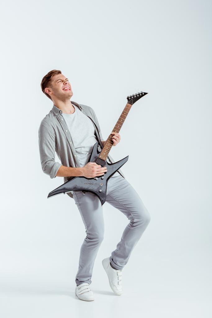 ενθουσιασμένος ο άνθρωπος, με γκρίζα ρούχα παίζοντας ηλεκτρική κιθάρα σε γκρι φόντο - Φωτογραφία, εικόνα