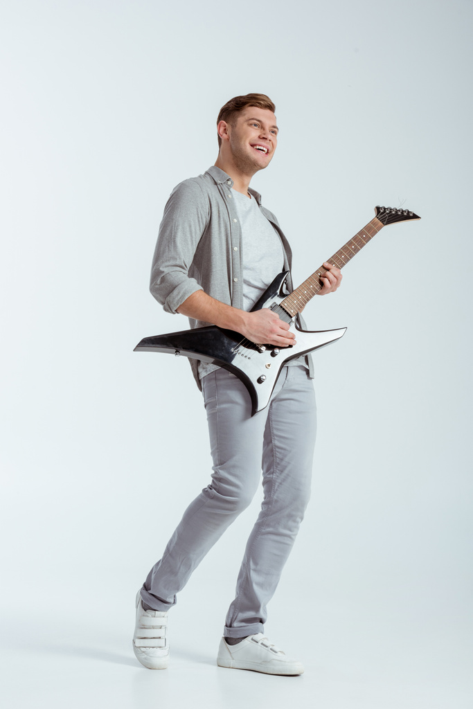 excité homme souriant en vêtements gris jouer de la guitare électrique sur fond gris
 - Photo, image