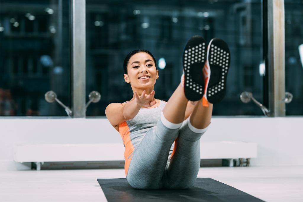 beautiful asian sportswoman smiling and training on fitness mat in sports center - Photo, Image