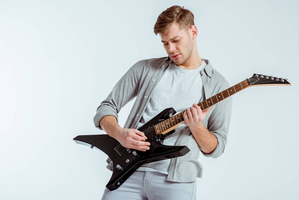 gutaussehender, fokussierter Mann in grauer Kleidung, der vereinzelt E-Gitarre auf Grau spielt - Foto, Bild