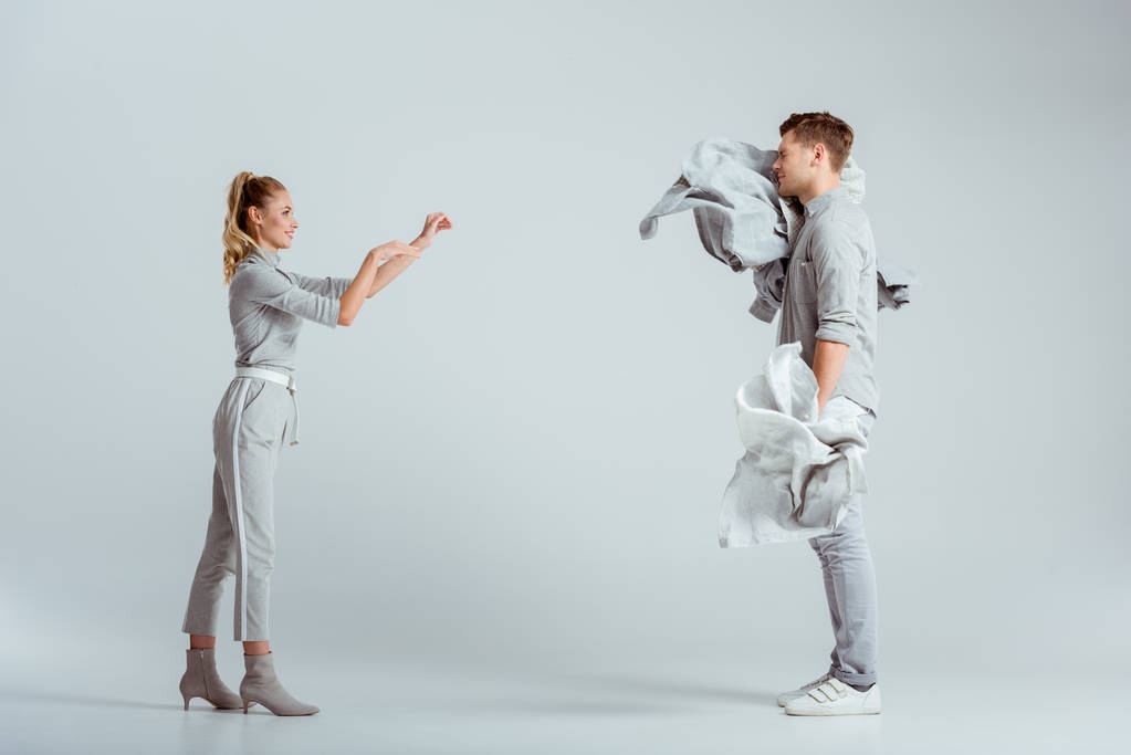 attractive woman throwing pile of clothes at man on grey background - Photo, Image