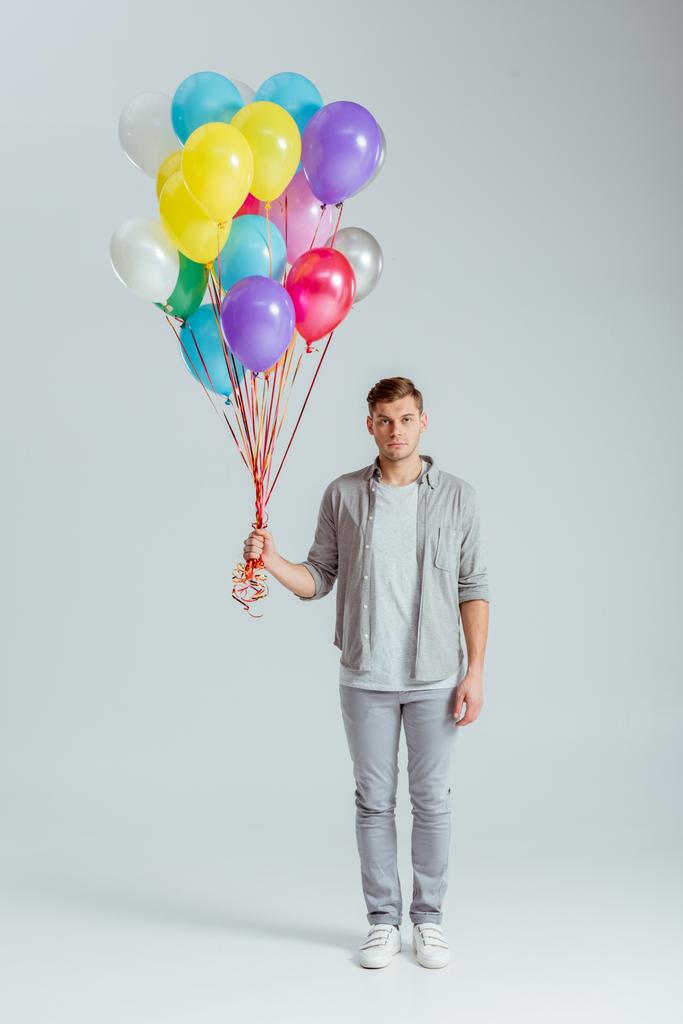 man in grey clothing holding bundle of colorful balloons on grey background - Photo, Image