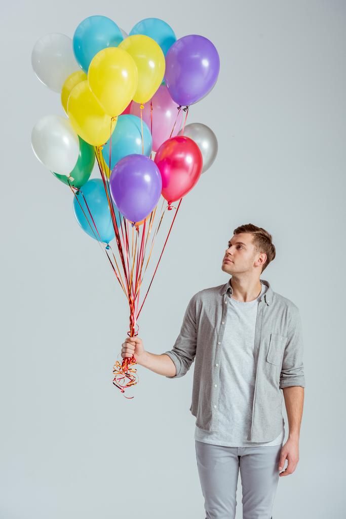 όμορφος άνδρας κρατώντας δέσμη από πολύχρωμα μπαλόνια σε γκρίζο φόντο - Φωτογραφία, εικόνα