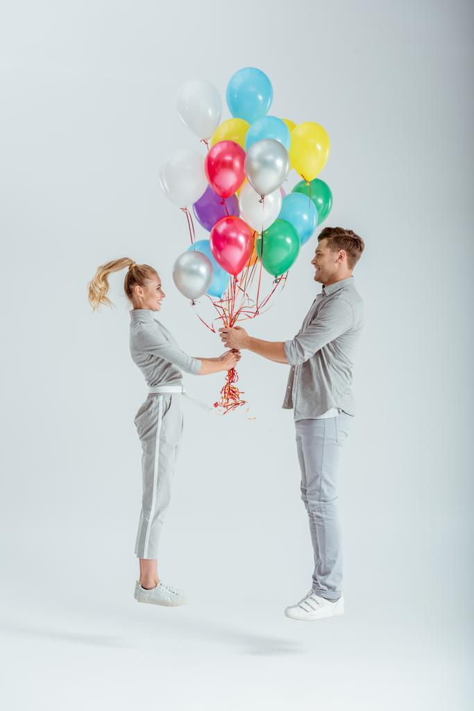 пара в серой одежде прыгает с пучком разноцветных воздушных шаров на сером фоне
 - Фото, изображение