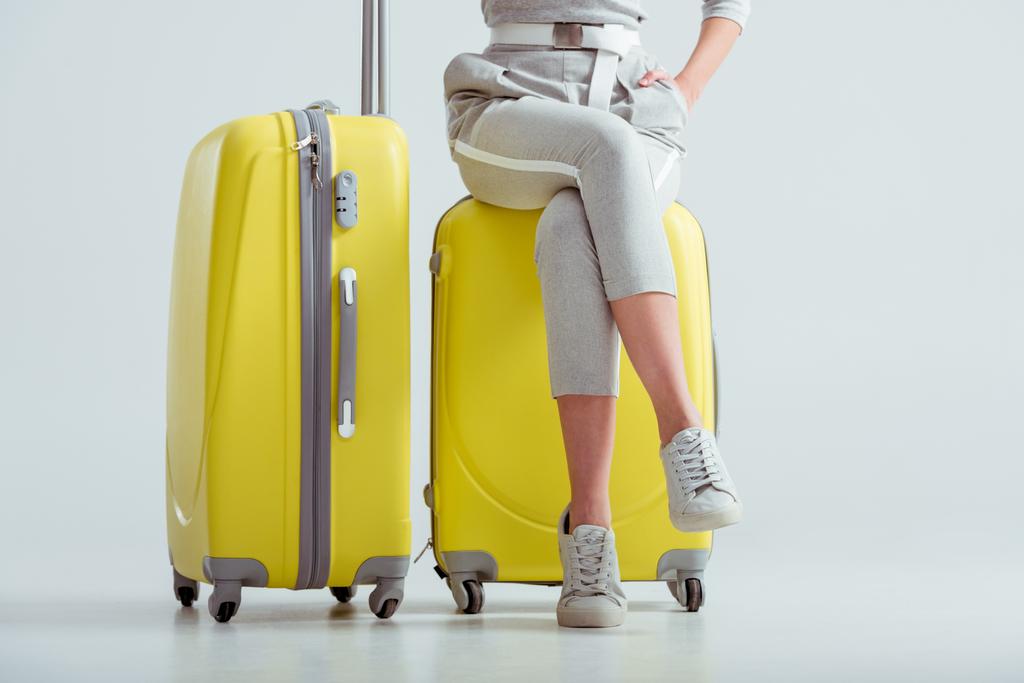 przycięte widzenia kobieta siedzi na walizkach ze skrzyżowanymi nogami na szarym tle, podróżować pojęcie - Zdjęcie, obraz