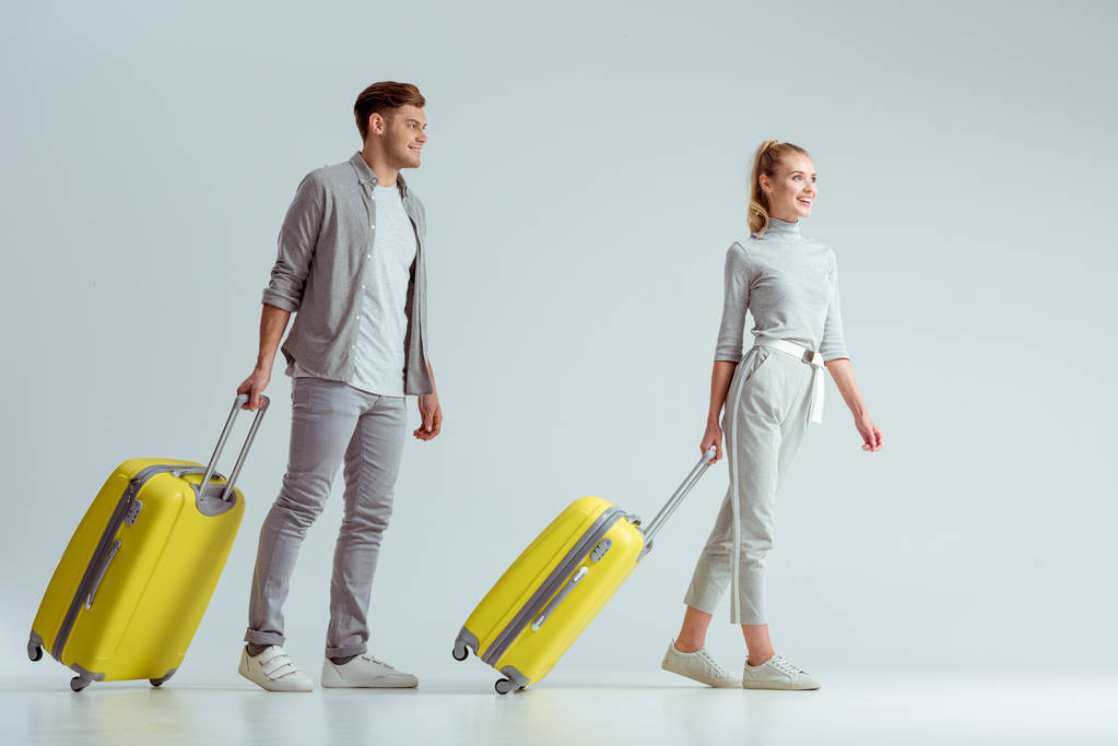 sorrindo casal carregando malas amarelas em fundo cinza, conceito de viagem
 - Foto, Imagem