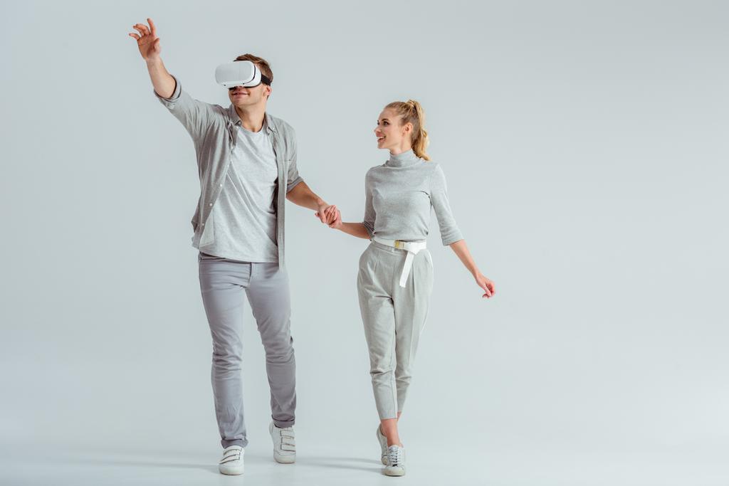 couple holding hands while man experiencing virtual reality and gesturing on grey background - Photo, Image