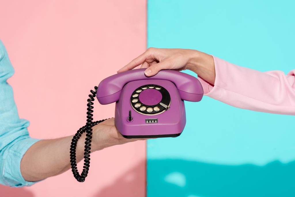 vista ritagliata di uomo e donna in possesso di viola vintage telefono su sfondo rosa e blu
 - Foto, immagini