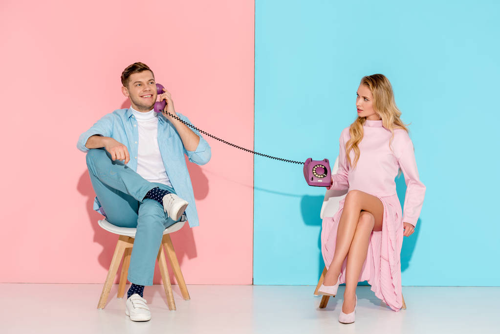 dissatisfied woman holding purple vintage telephone while smiling man talking with pink and blue background - Photo, Image