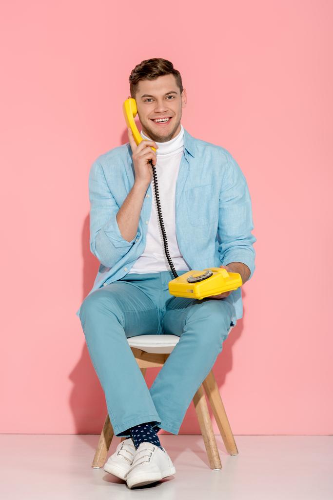homme souriant assis et parlant sur un téléphone vintage jaune avec fond rose
 - Photo, image