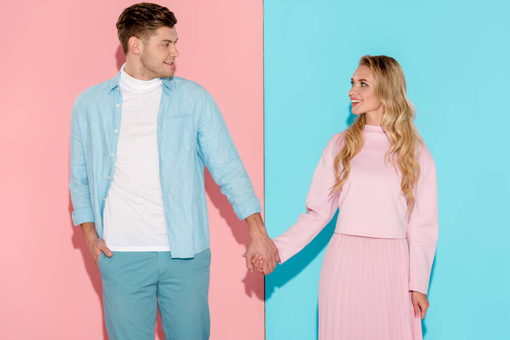 happy couple holding hands and looking at each other on pink and blue background - Photo, Image