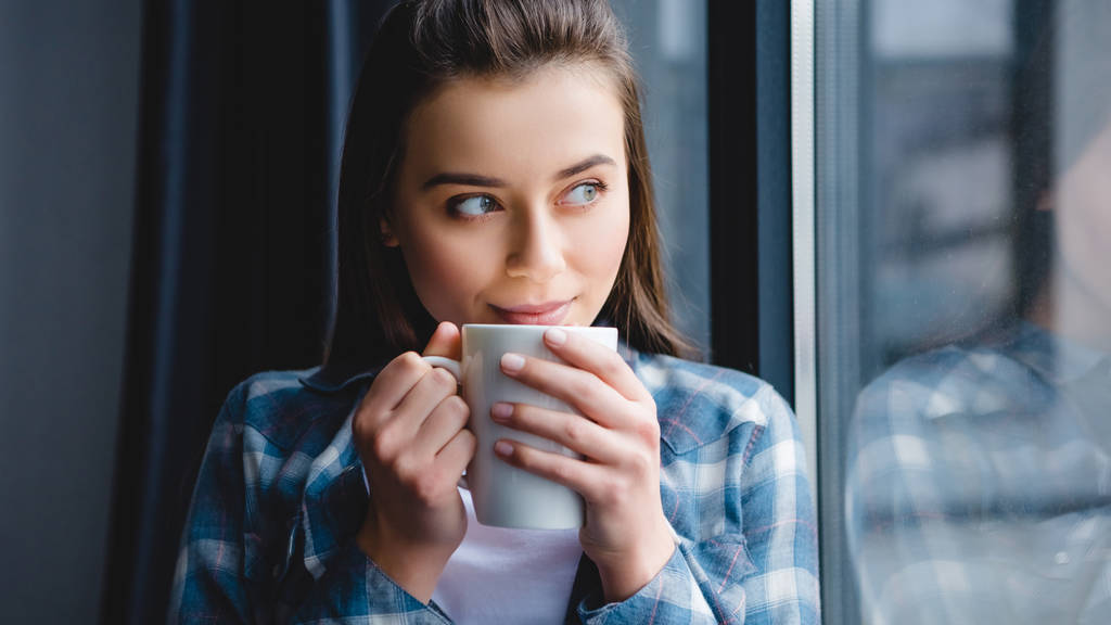 schönes glückliches Mädchen, das Tee trinkt und zum Fenster schaut  - Foto, Bild