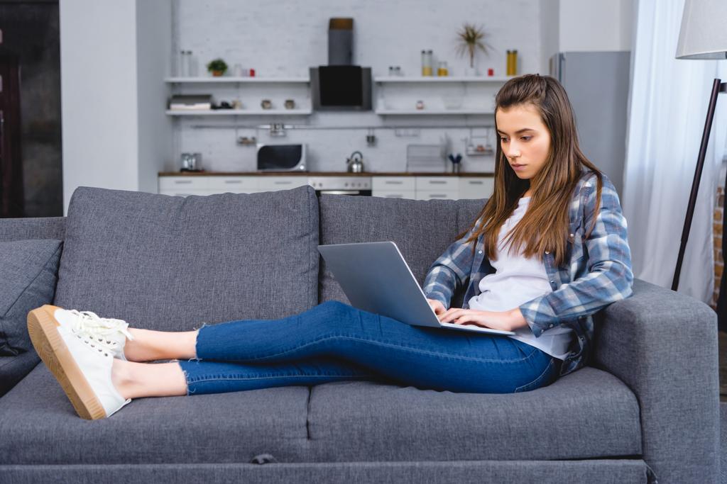 täyspitkä näkymä kaunis nuori nainen istuu sohvalla ja kannettavan tietokoneen
 - Valokuva, kuva