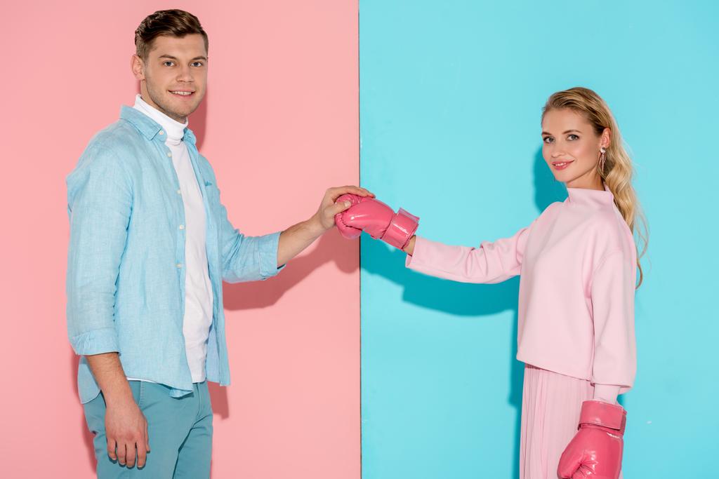 man looking at camera and holding boxing glove of woman on pink and blue background - Photo, Image