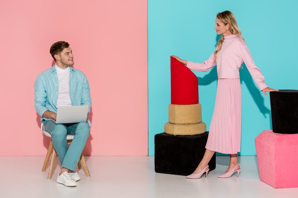 女性がマニキュアと口紅モデル男の椅子に座って、ピンクとブルーの背景にノート パソコンを使用しながらポーズ - 写真・画像