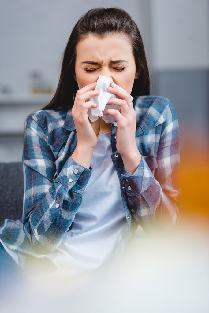 selective focus of young woman with allergy blowing nose in facial tissue - Photo, Image