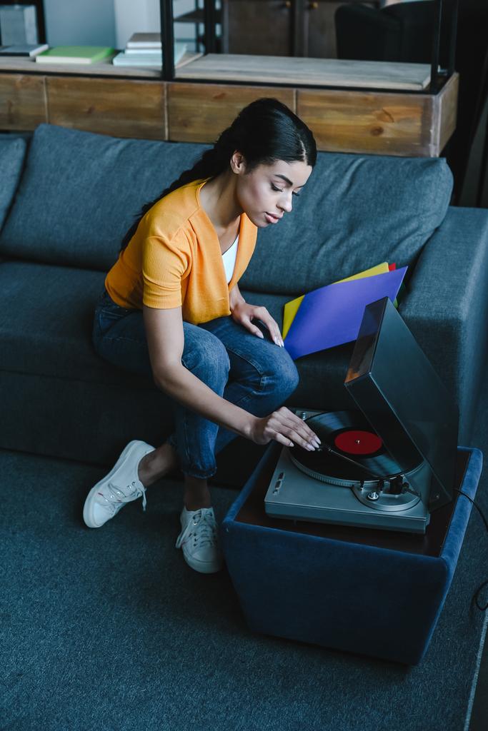 high angle view of beautiful mixed race girl in orange shirt turning on gramophone with retro vinyl at home - Photo, Image