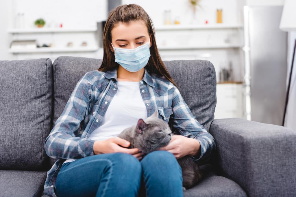 κορίτσι στην ιατρική μάσκα κρατώντας γάτα και που πάσχουν από αλλεργία στο σπίτι   - Φωτογραφία, εικόνα
