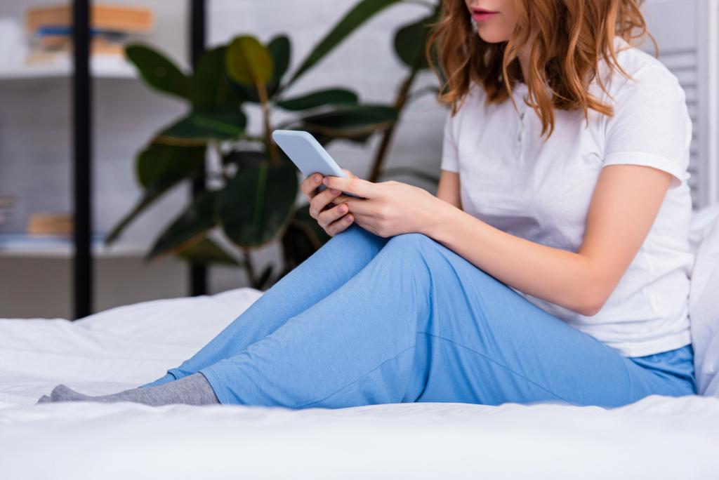 image recadrée d'une femme aux cheveux roux reposant au lit et utilisant un smartphone à la maison le week-end
 - Photo, image