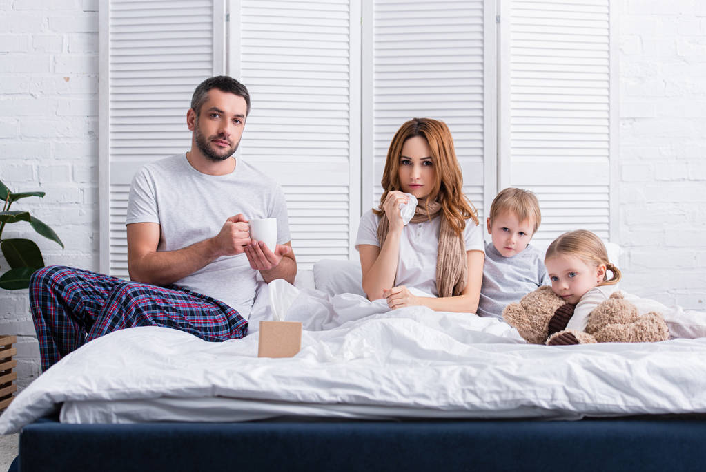 aviomies ja lapset tukevat sairasta äitiä makuuhuoneessa, katsot kameraa
 - Valokuva, kuva