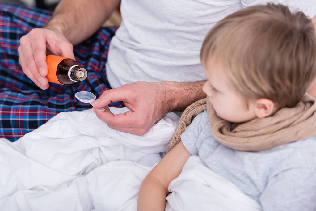 cropped image of father taking care of sick son in bedroom and pouring medicines in spoon - Photo, Image