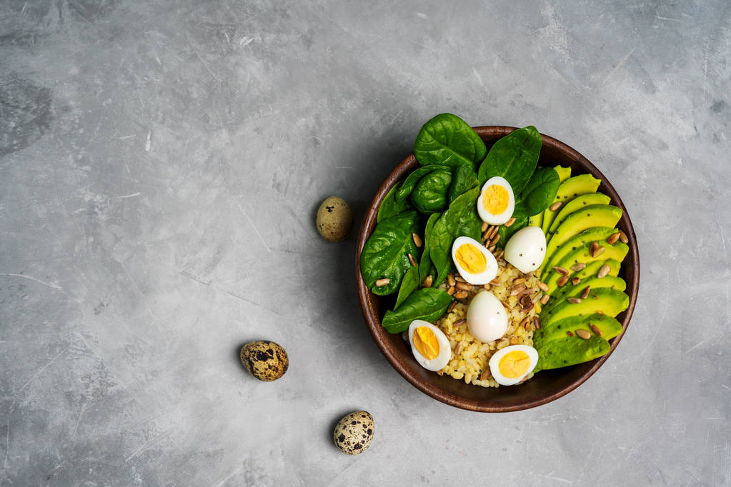 Vista dall'alto dell'insalata con bulgur, spinaci, avocado e uova di quaglia in una ciotola di legno su sfondo di cemento
 - Foto, immagini