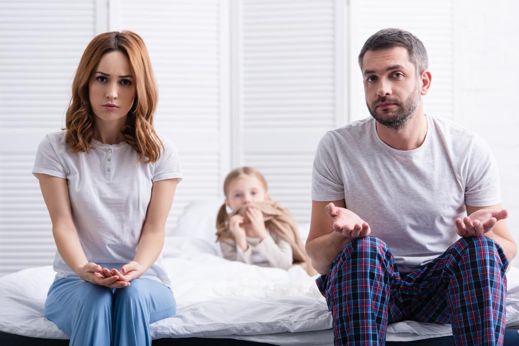 huolestuneet vanhemmat istuvat lähellä sairasta tytärtä makuuhuoneessa ja katsovat kameraa, isä osoittaa kohauttavaa elettä
 - Valokuva, kuva