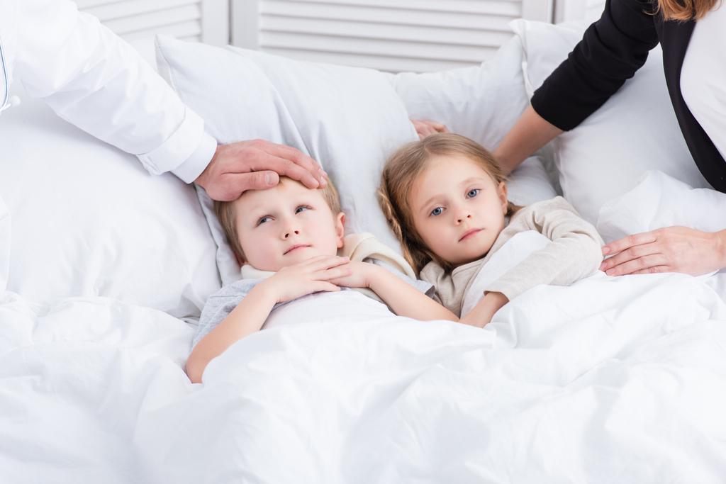 imagen recortada de pediatra y madre cuidando niños enfermos en el dormitorio
 - Foto, Imagen
