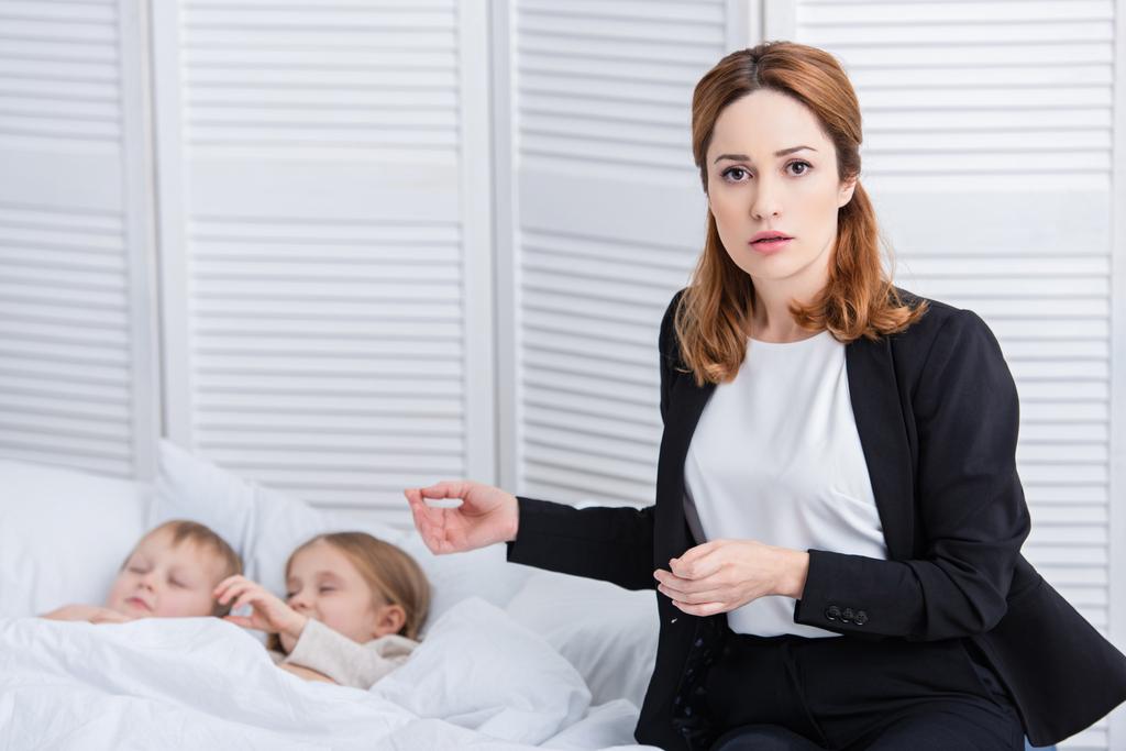 беспокойная мать стоит рядом с двумя больными детьми и смотрит в камеру в спальне
 - Фото, изображение
