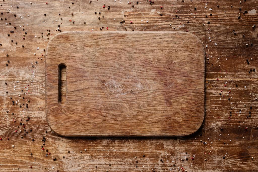 top view of cutting board on wooden table with scattered peppercorns - Photo, Image
