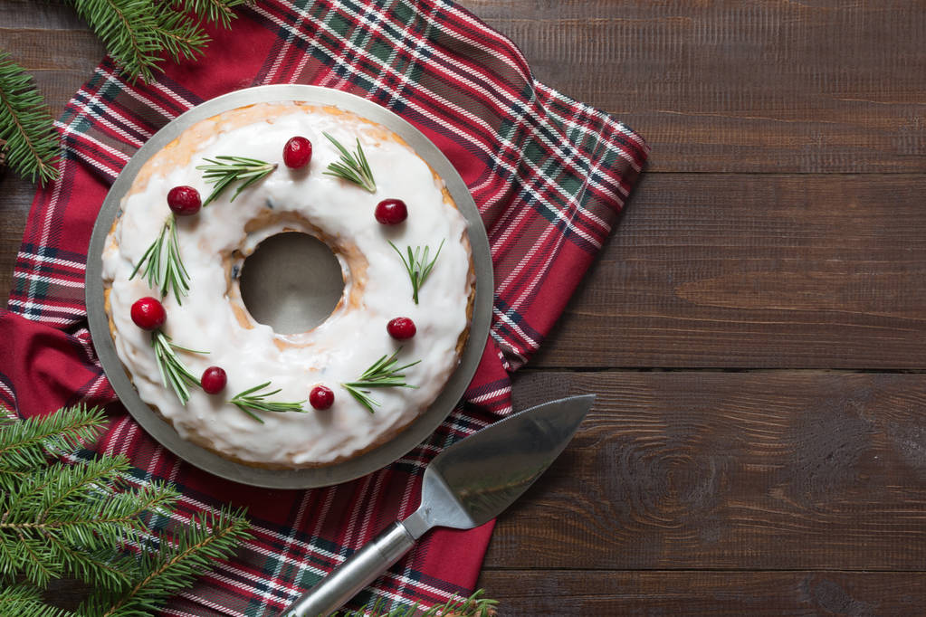 Tarta tradicional de Navidad casera decorada con bayas rojas del Norte y romero en plato y tablero de madera. Polvo con azúcar glas
. - Foto, imagen