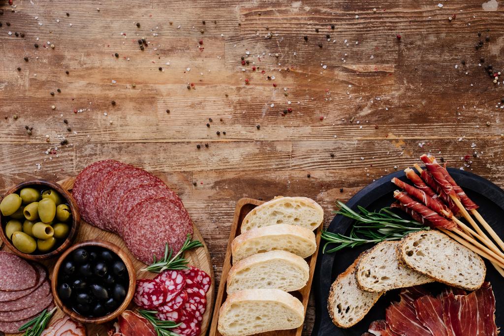bovenaanzicht van snijplanken met olijven, breadsticks, ham, salami, brood en kruiden op houten vintage tafel - Foto, afbeelding