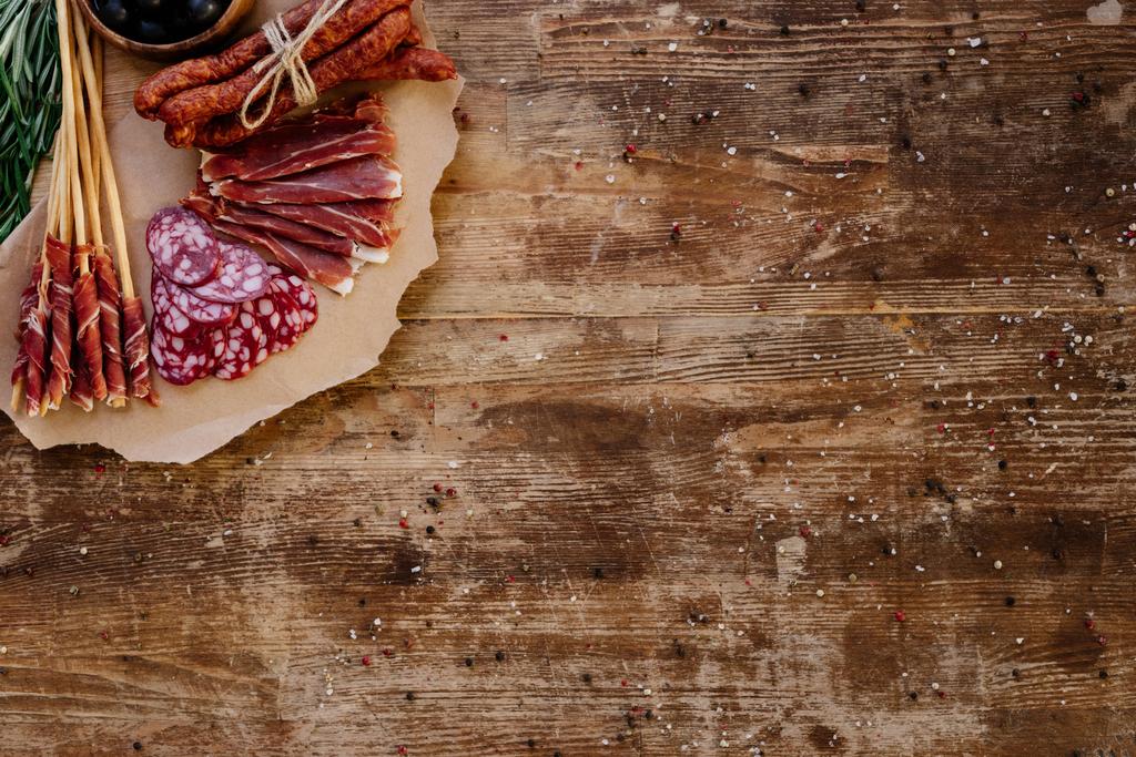 top view of cutting board with sliced prosciutto, salami and smoked sausages on wooden vintage table  with scattered spices - Photo, Image