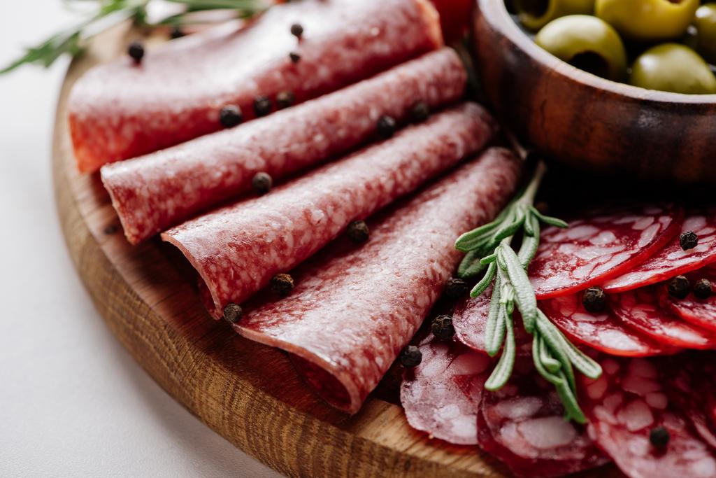 Close-up van heerlijke gesneden salami met rozemarijn en peperkorrels op houten snijplank - Foto, afbeelding