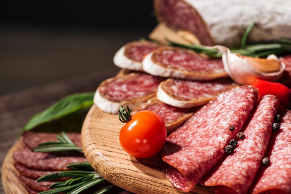 close up view of wooden cutting boards with delicious sliced salami, herbs and vegetables - Photo, Image
