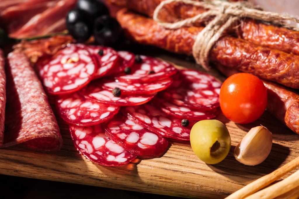 close up view of wooden cutting boards with delicious smoked sausages, vegetables and sliced salami - Photo, Image
