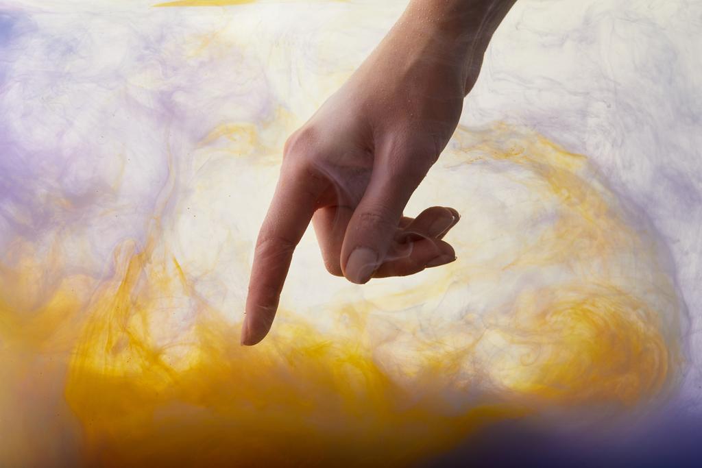 női kéz a víz, a narancs és lila festék kavarog - Fotó, kép