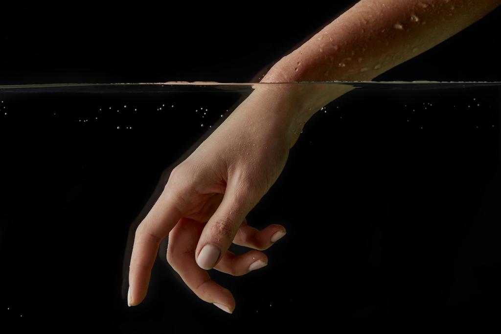 Frau steckt Hand in klares Wasser isoliert auf schwarz  - Foto, Bild