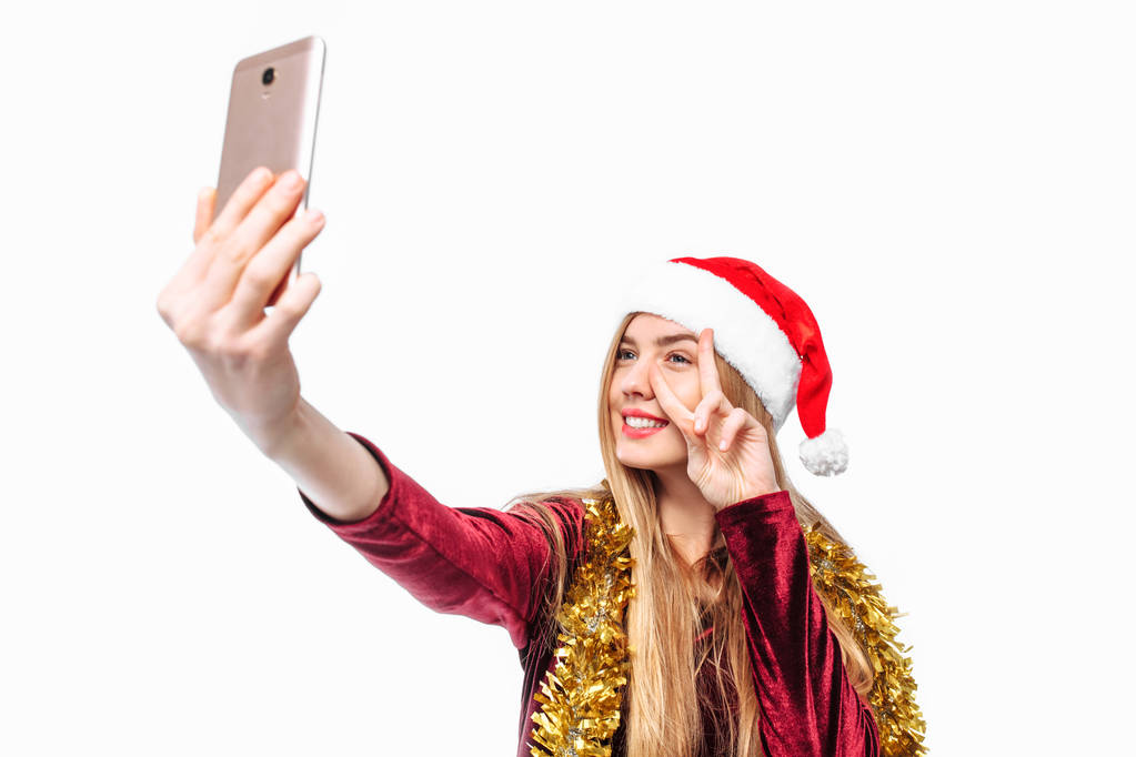 Glückliche Frau mit Weihnachtsmütze und Kleid, erschießt sich selbst, per Smartphone. auf weißem Hintergrund - Foto, Bild