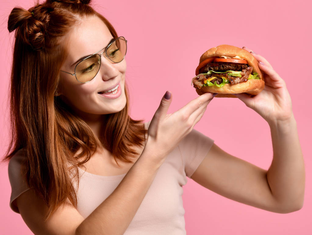 Крупним планом портрет голодної молодої жінки, що їсть бургер ізольовані на рожевому фоні
 - Фото, зображення