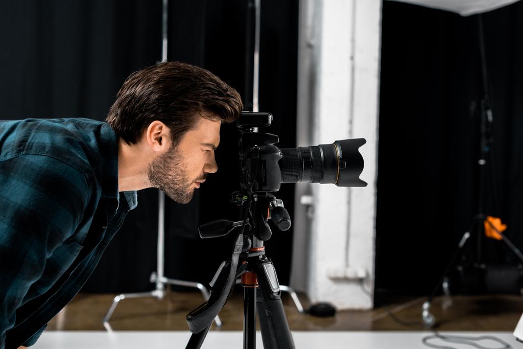 vue latérale du jeune photographe travaillant avec un appareil photo professionnel en studio
   - Photo, image