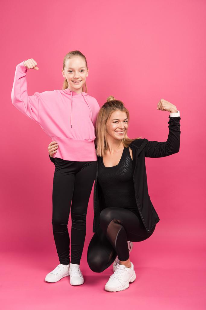 starke Mutter und Tochter zeigen muskulösen Bizeps auf rosa - Foto, Bild